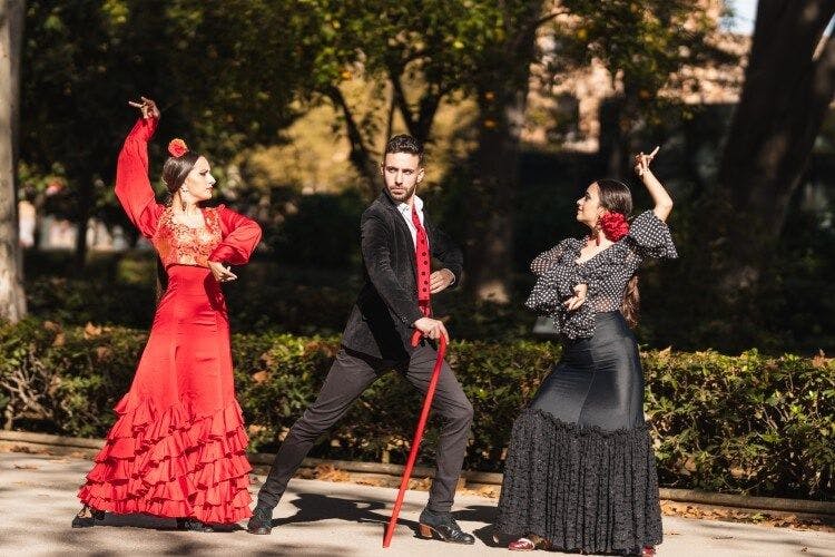 Three flamenco dancers, two women and one man, in traditional dress dancing Flamenco in a Spanish park