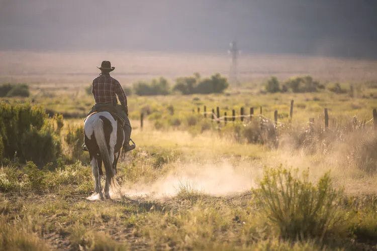 A man on horseback in a cowboy hat rides across dusty plains in Texas
