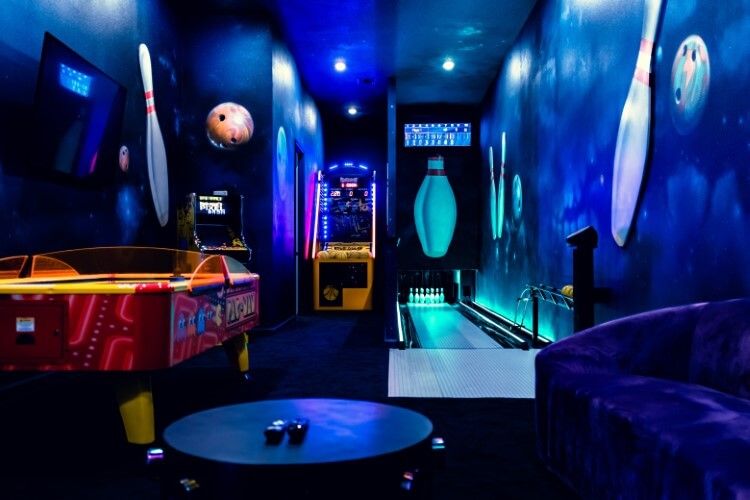 A bowling alley and game room in Villatel Village 15, with navy=painted wall, a glowing ten pin bowling alley and an air hockey table