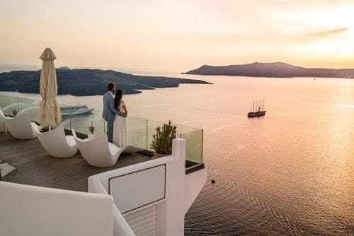 A couple stand on the balcony of a Greek villa looking out of the sea