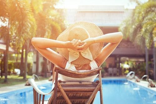 A woman in a large straw hat sits in a sun lounger by a pool