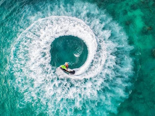 Aerial shot of someone doing donuts in the sea on a jet ski