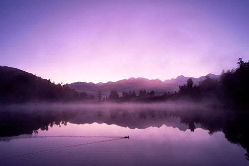 A purple sky at dawn with mountains and a still lake