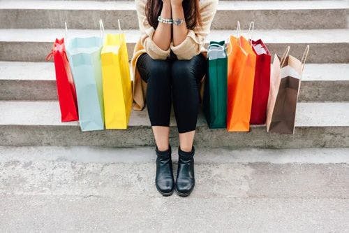 A woman sits on a step with colorful paper shopping bags