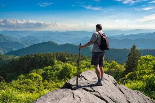 A man with a hiking pole stands a top of a rocky mountain in North Carolina
