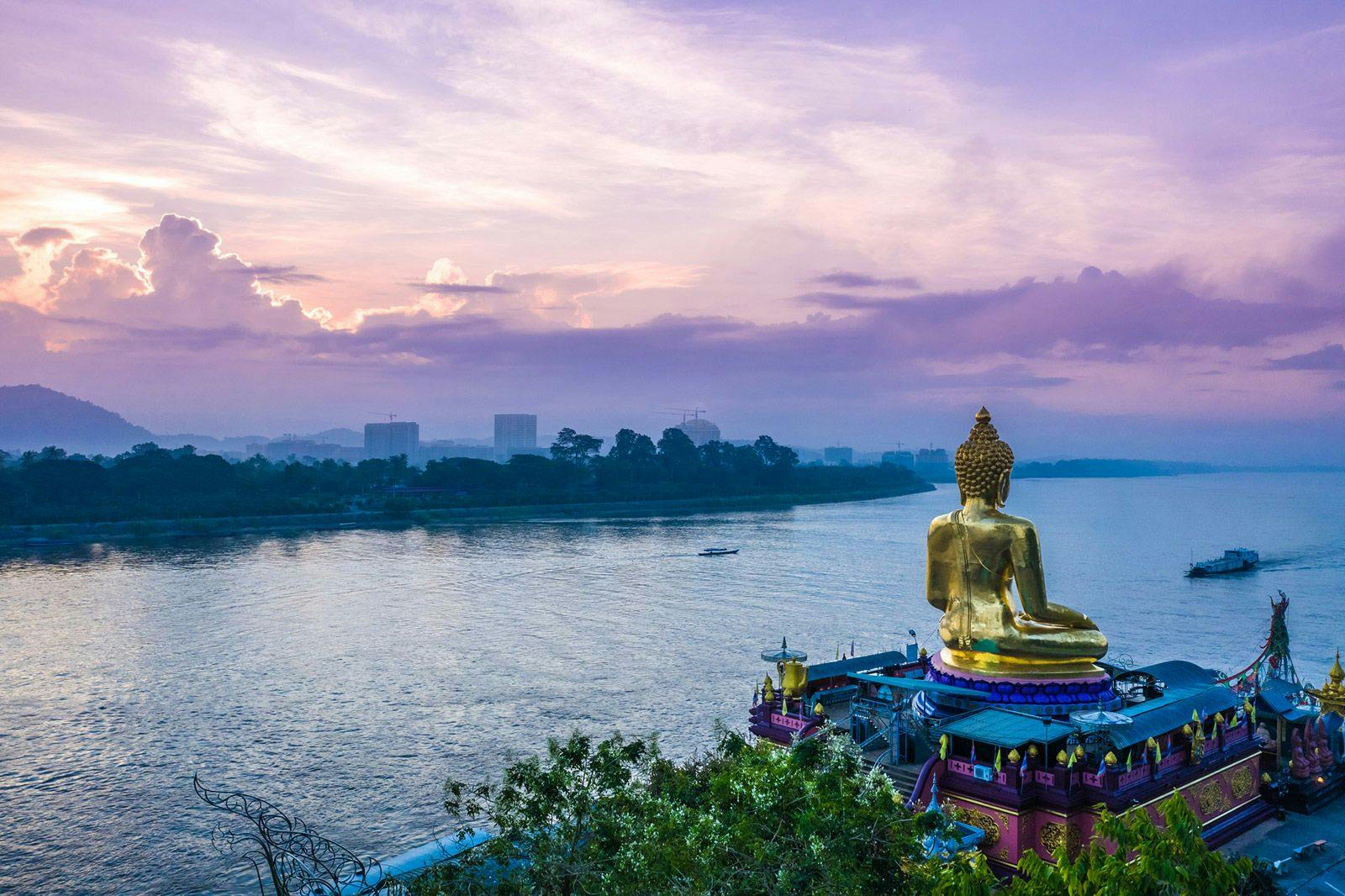A golden buddah siting on a hill overlooking the Mekong River in Thailand