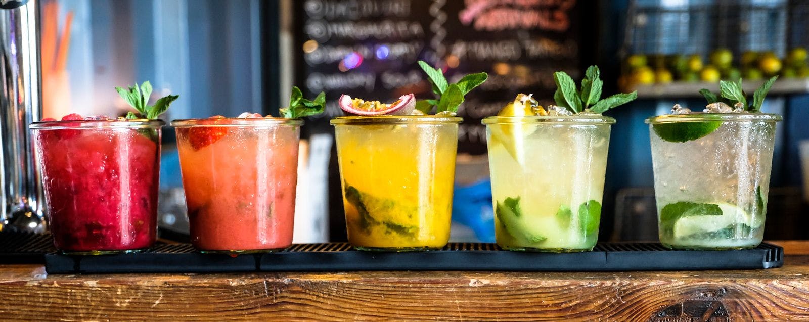 A line of rum cocktails in various colors on a wooden bar