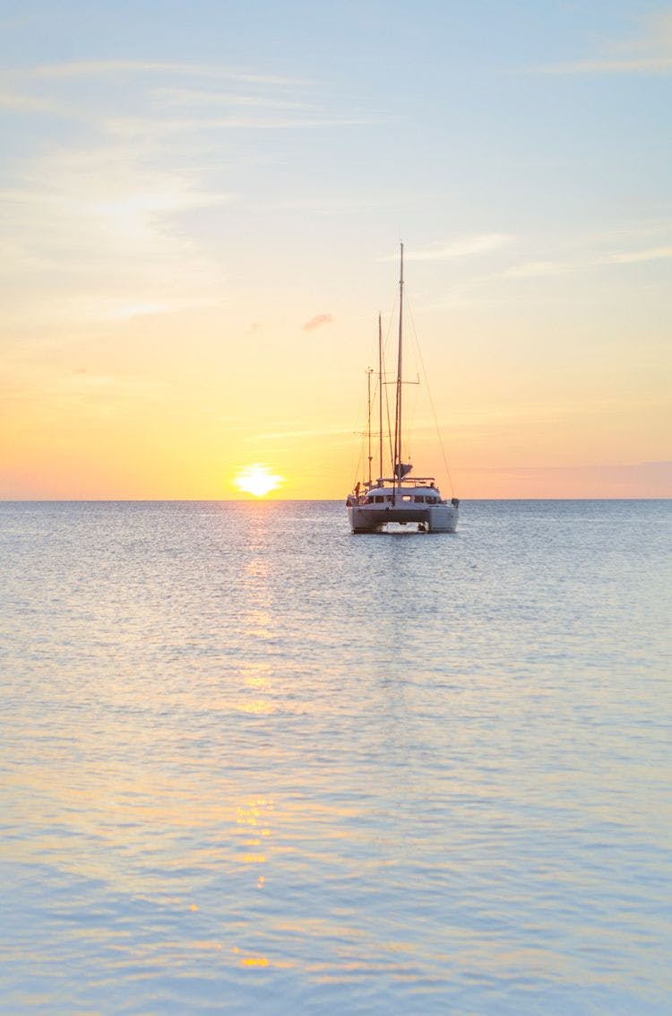 A yacht sailing towards a sunset on a flat sea