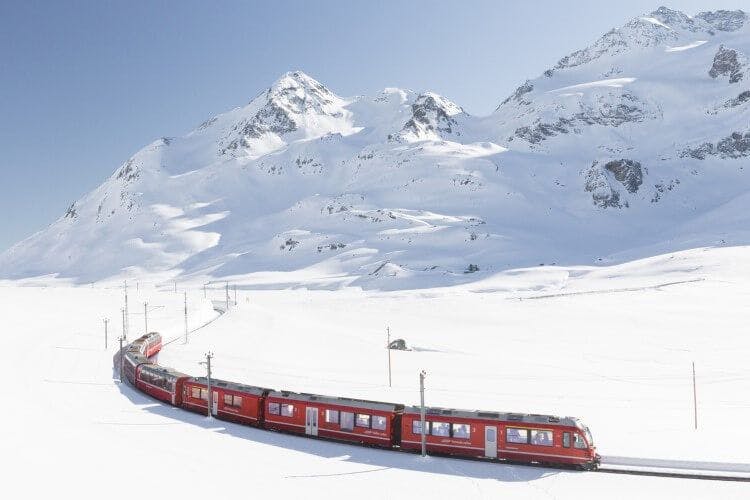 A red scenic train traveling through snowy mountains in Switzerland