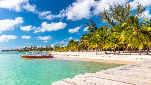 White sand palm-fringed beach with jetty and sailboat in the Dominican Republic