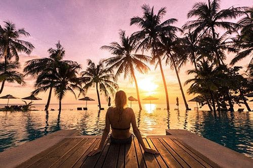 A woman sitting by a pool in the Caribbean at sunset