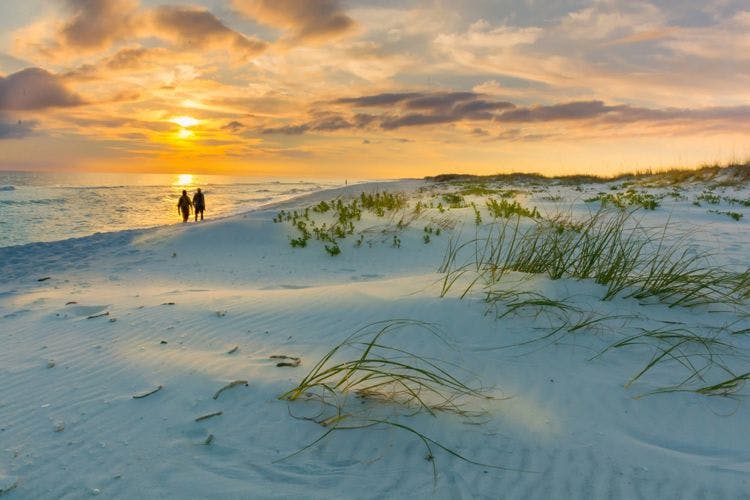 Two people walk along a white sand beach at sunset
