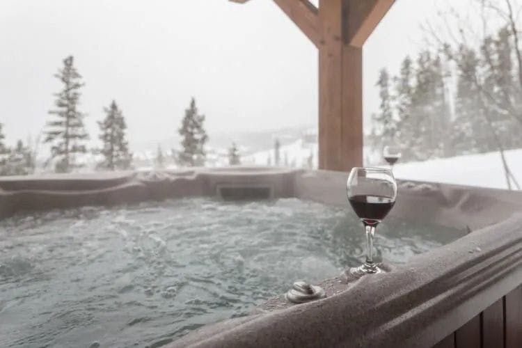 Big Sky 8 cabin hot tub with view of snowy mountains a glass of red wine on the side