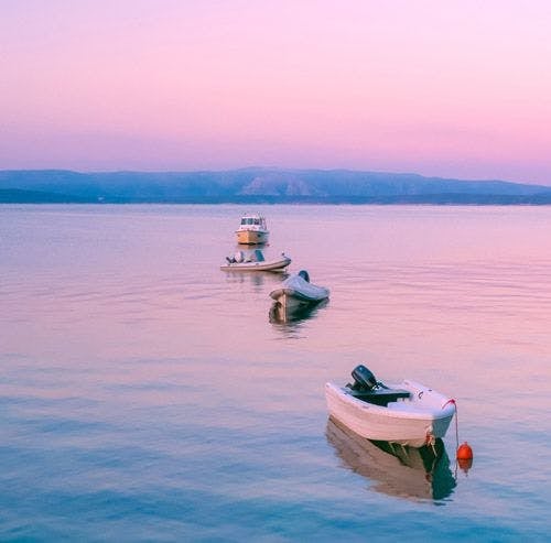 Three small boats moored in the water with a pink sunset sky