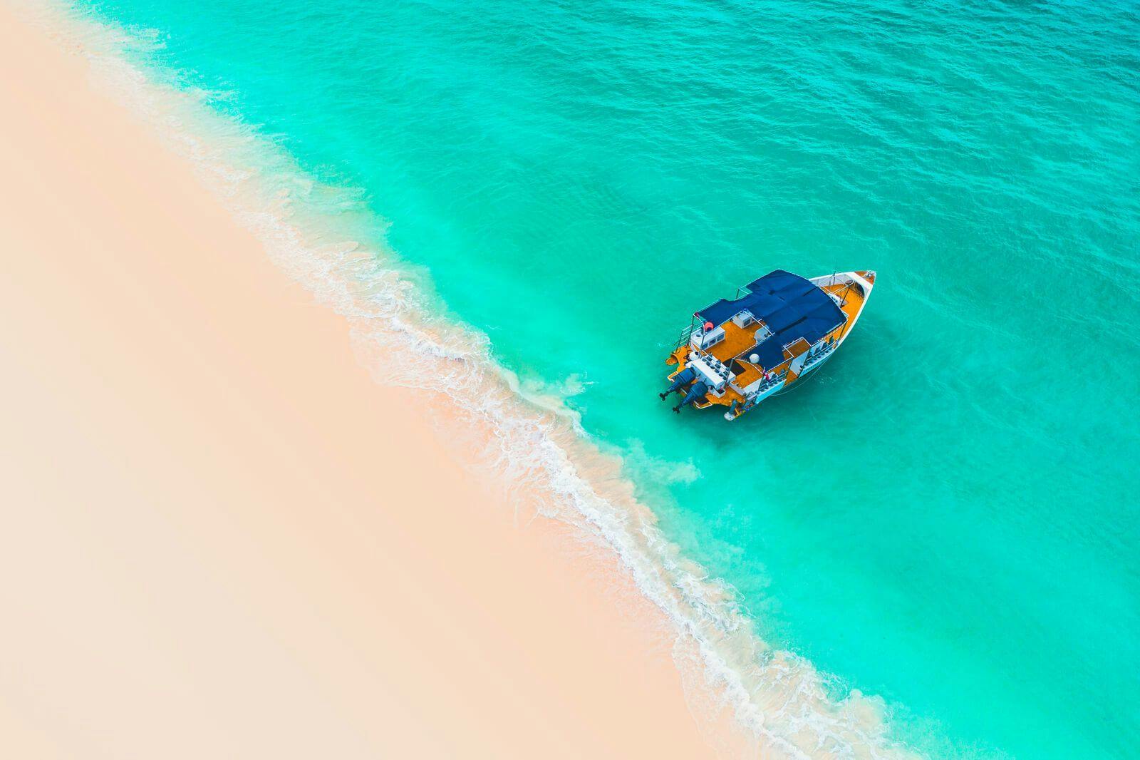 Small boat in water by white sand beach
