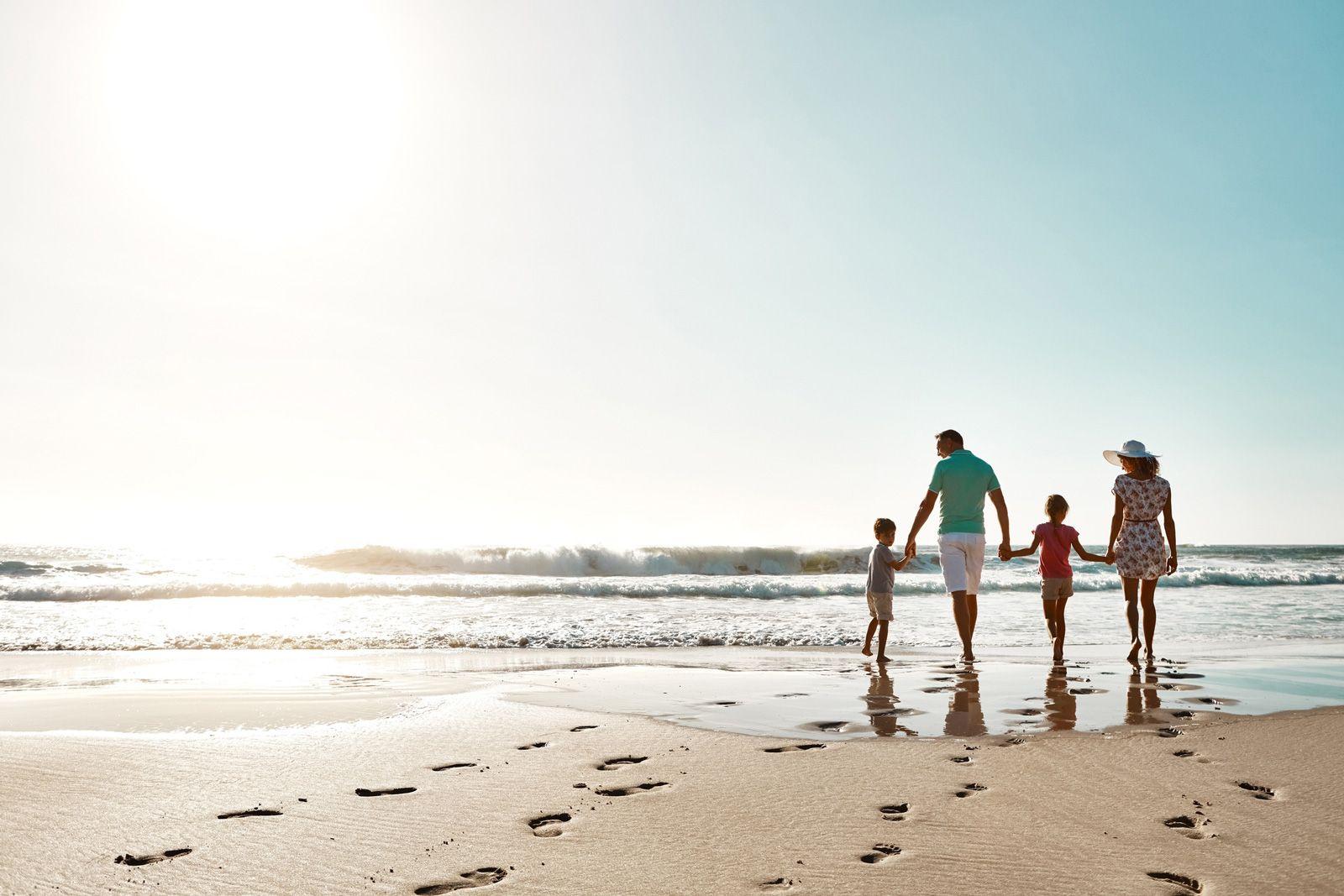 A family walking hand in hand along white sand