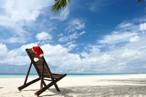 A Santa hat on a wooden chair on a white sand beach