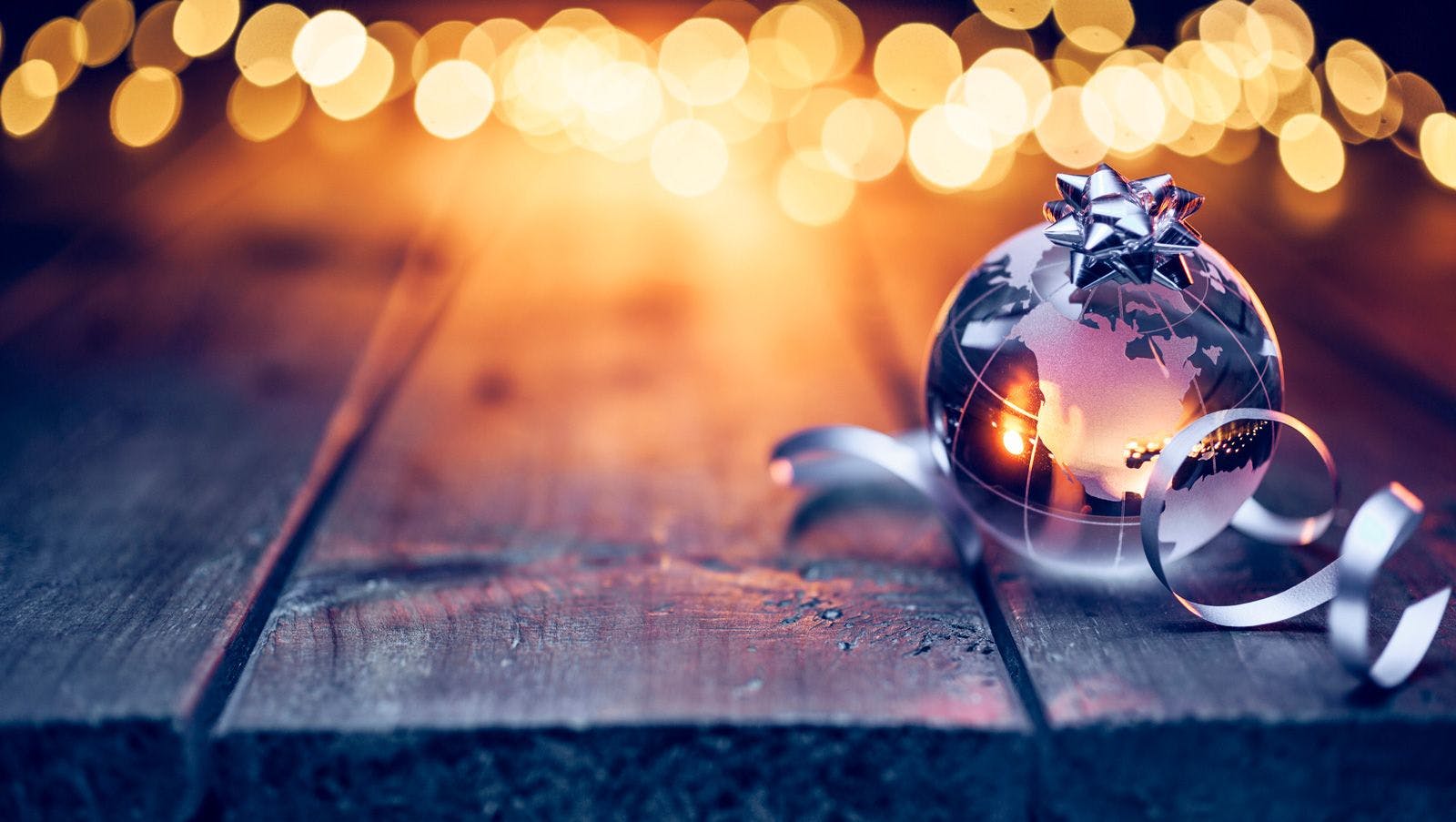A glass globe with a silver ribbon with Christmas lights in the background