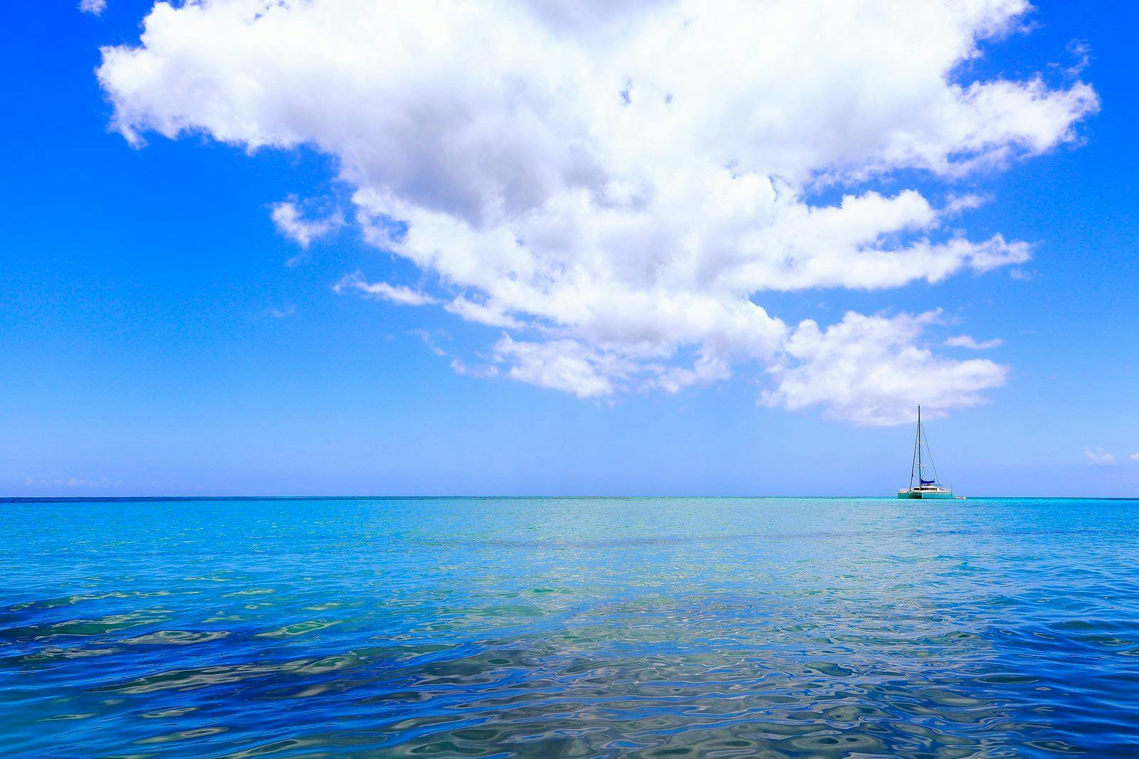 Sailboat on the horizon of blue sea in St Barts with white fluffy cloud overhead