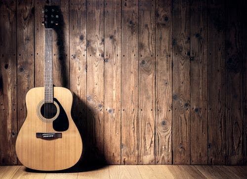 An acoustic guitar resting against a wooden wall