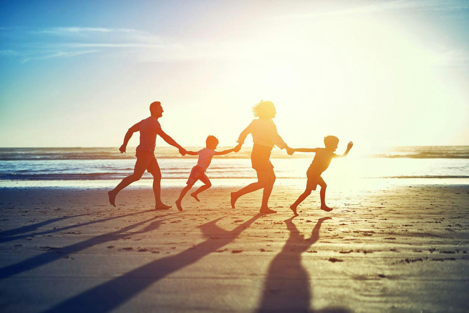 A family running across a beach at sunset