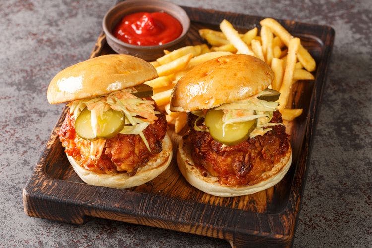 Two small chikcen burgers with fries on a wooden platter