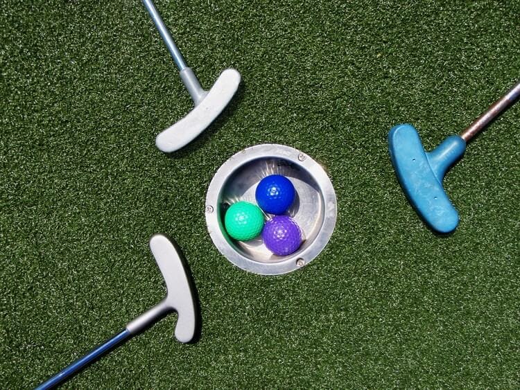 Three mini golf clubs arranged around a hole with three brightly colored golf balls in it