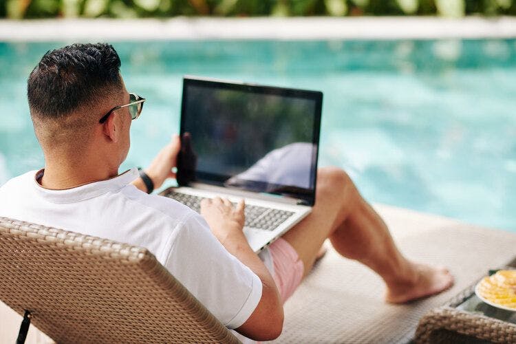 A man relaxing by the pool with a laptop