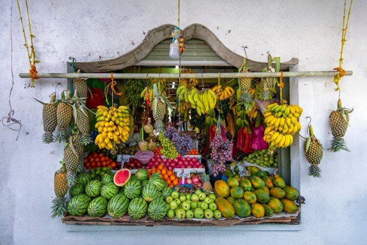 A colorful fruit stall in the Caribbean with fruit displayed including bananas, melons and avocados