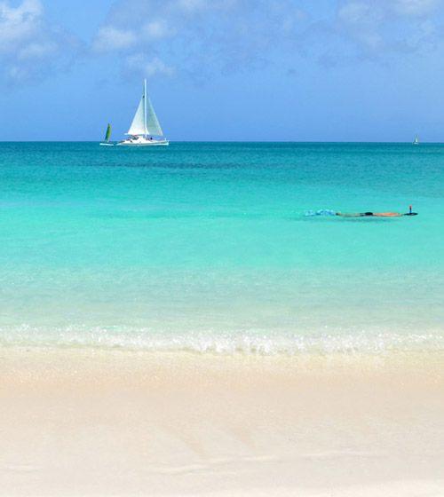 White sand beach with snorkeler and sail boat in the water