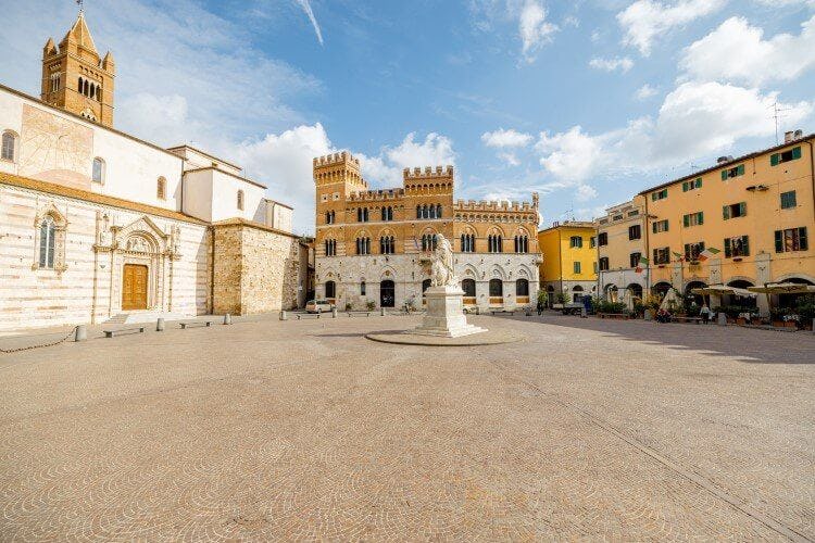 The town square in Grosseto with yellow and white buildings around a small plinth and statue in the center