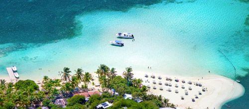 Overhead view of white sand beach with boats moored next to reef