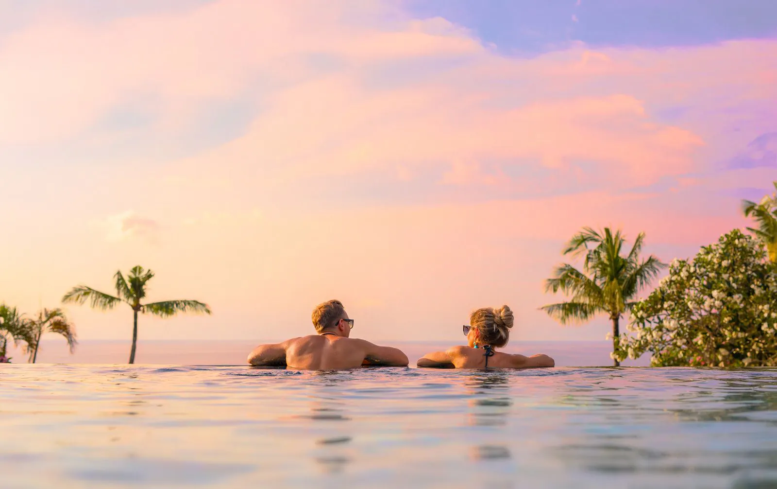 A couple at the edge of a pool watching a sunset over the sea
