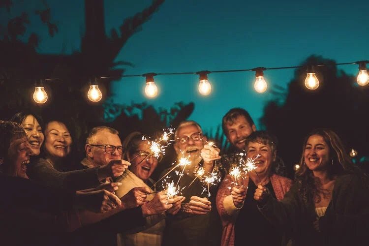 An extended family holding sparkles under lights in a garden