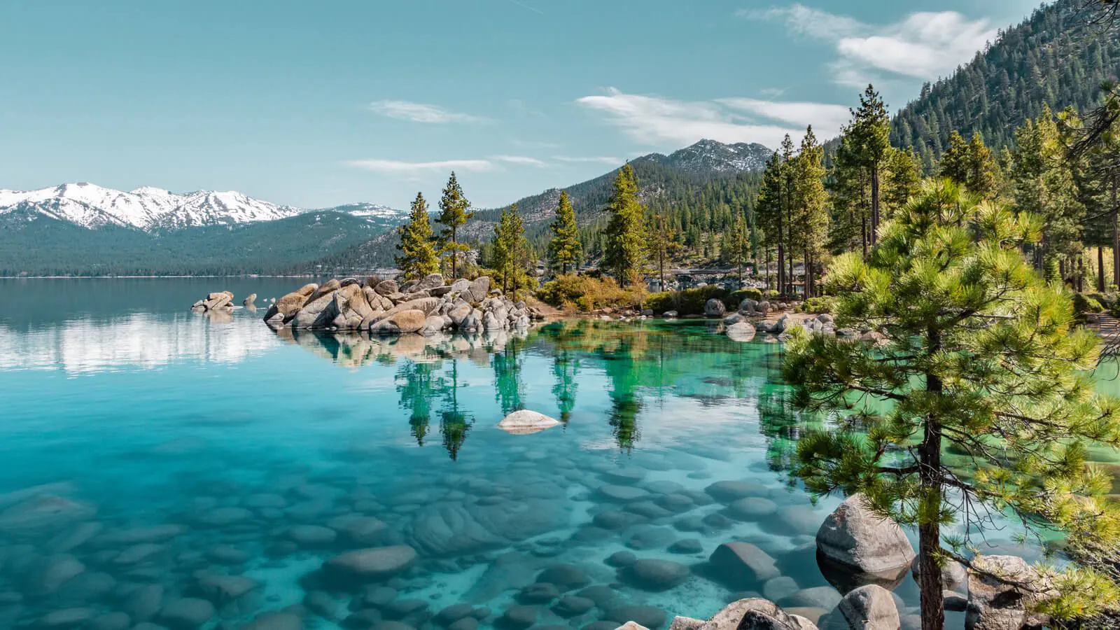 A view of Lake Tahoe with mountains and thick forest along the edge of the clear blue water
