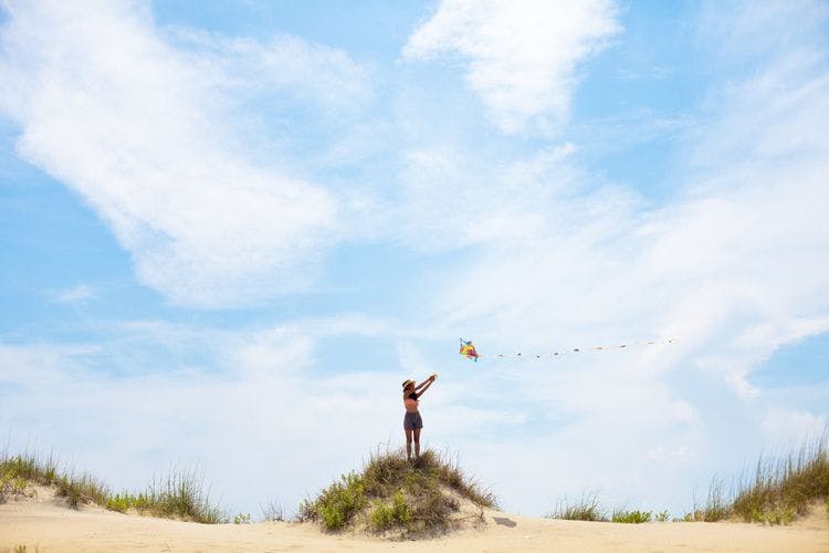 Lady flies a kite on a sand dune on a North Carolina beach