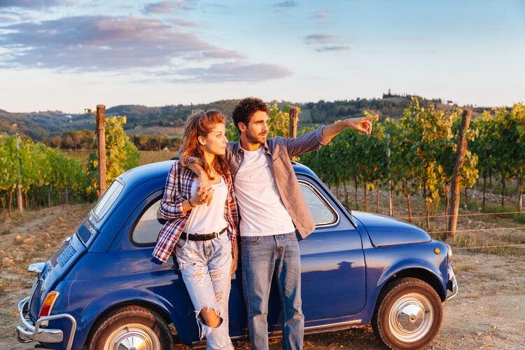 A couple stand next to their classic Fiat 500 and take in views of Tuscany
