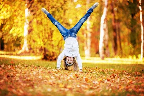 A girl doing a cartwheel through fall leaves on the ground