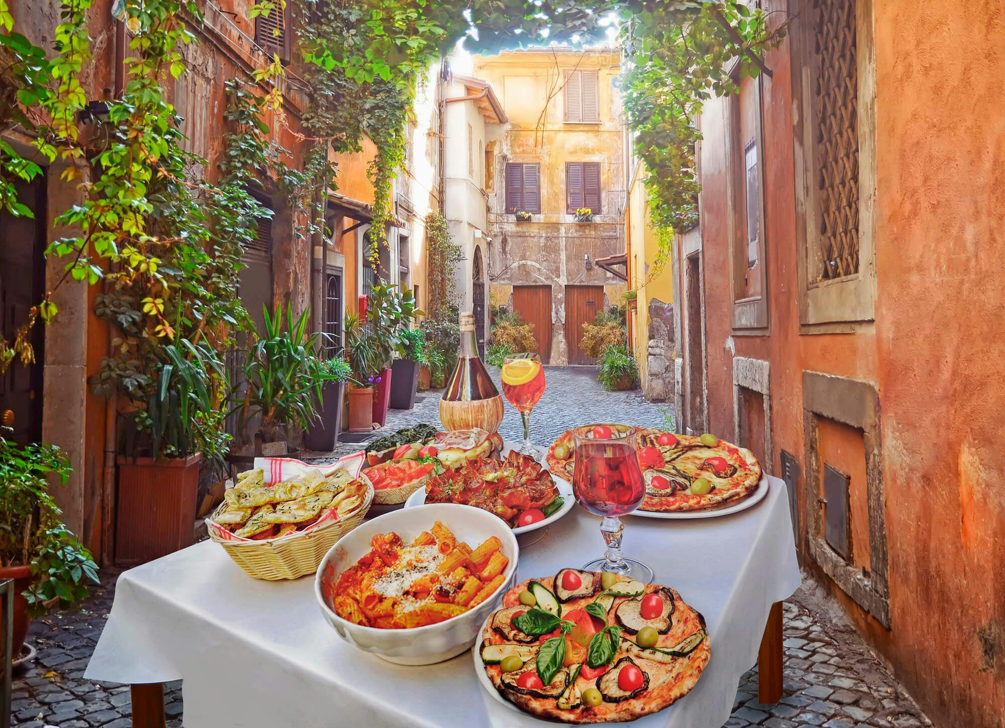 A table in an Italian street laid with dishes including pasta, pizza, and salad