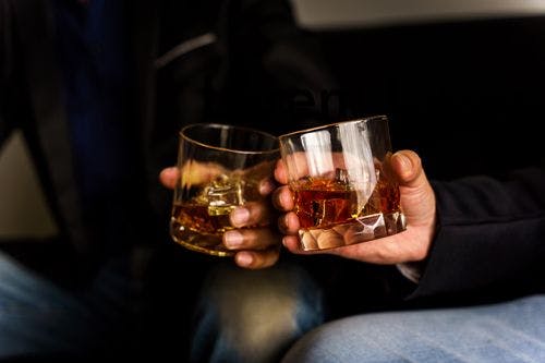 Two people clinking whiskey glasses