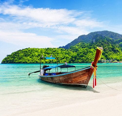 A traditional long tail fishing boat on the sand in Thailand