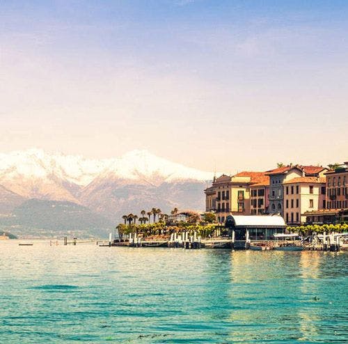Buildings on the edge of the water in Lake Como with snow-capped mountains in the background
