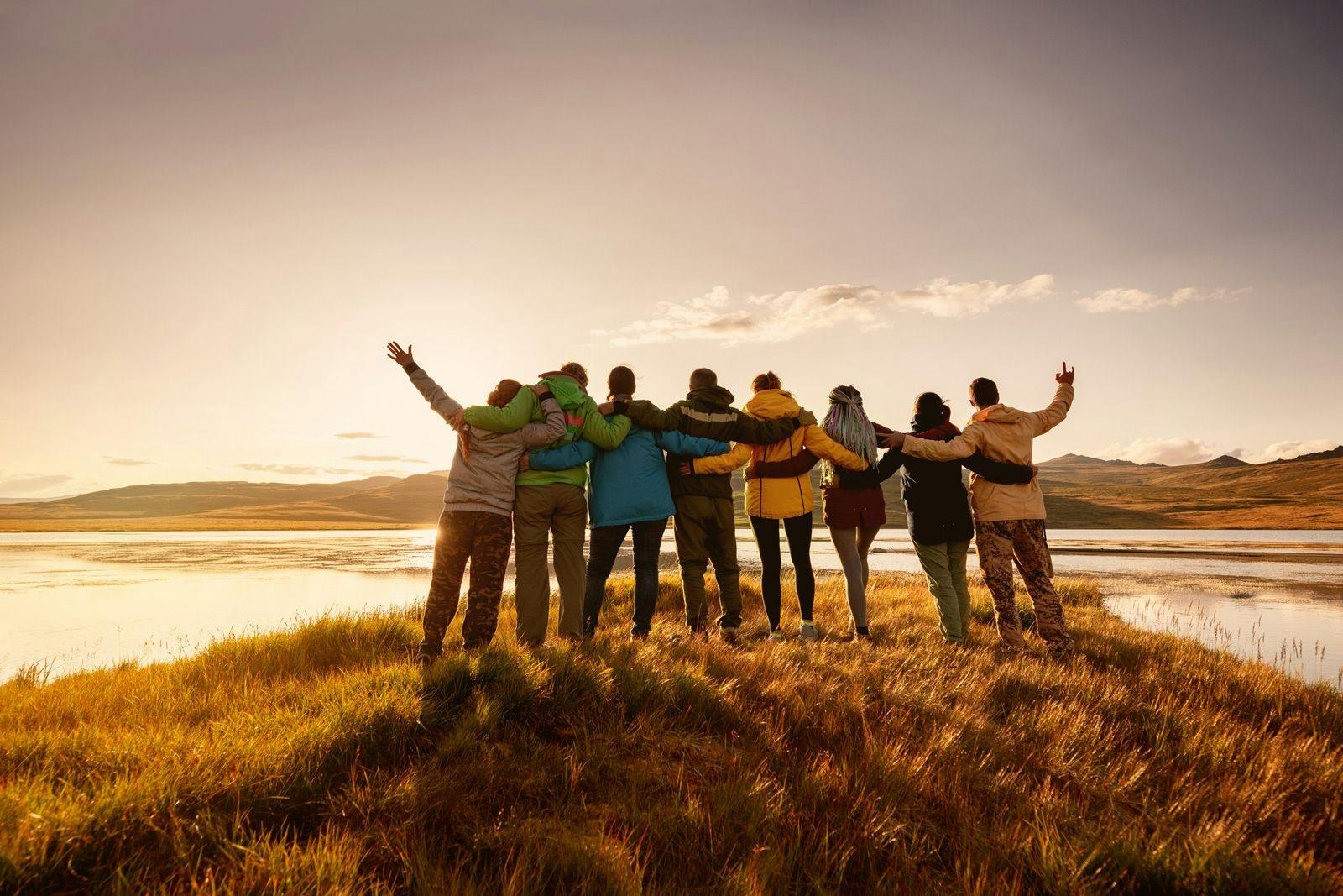A large group of people standing on a grassy hill watching a sunset