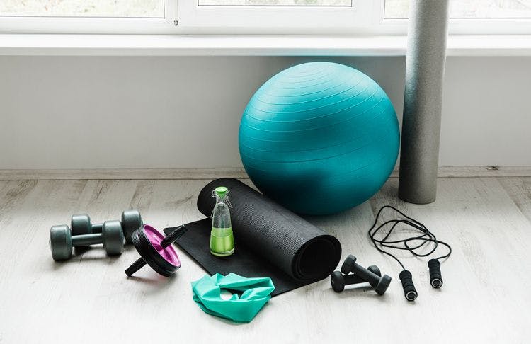 Stck image of gym equipment including yoga mat, balance ball, dumbbells and skipping rope