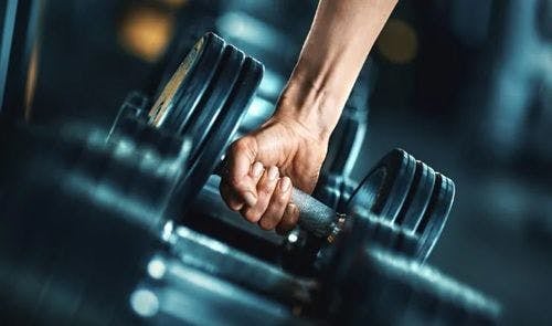 A hand reaching down to pick a dumbbell 