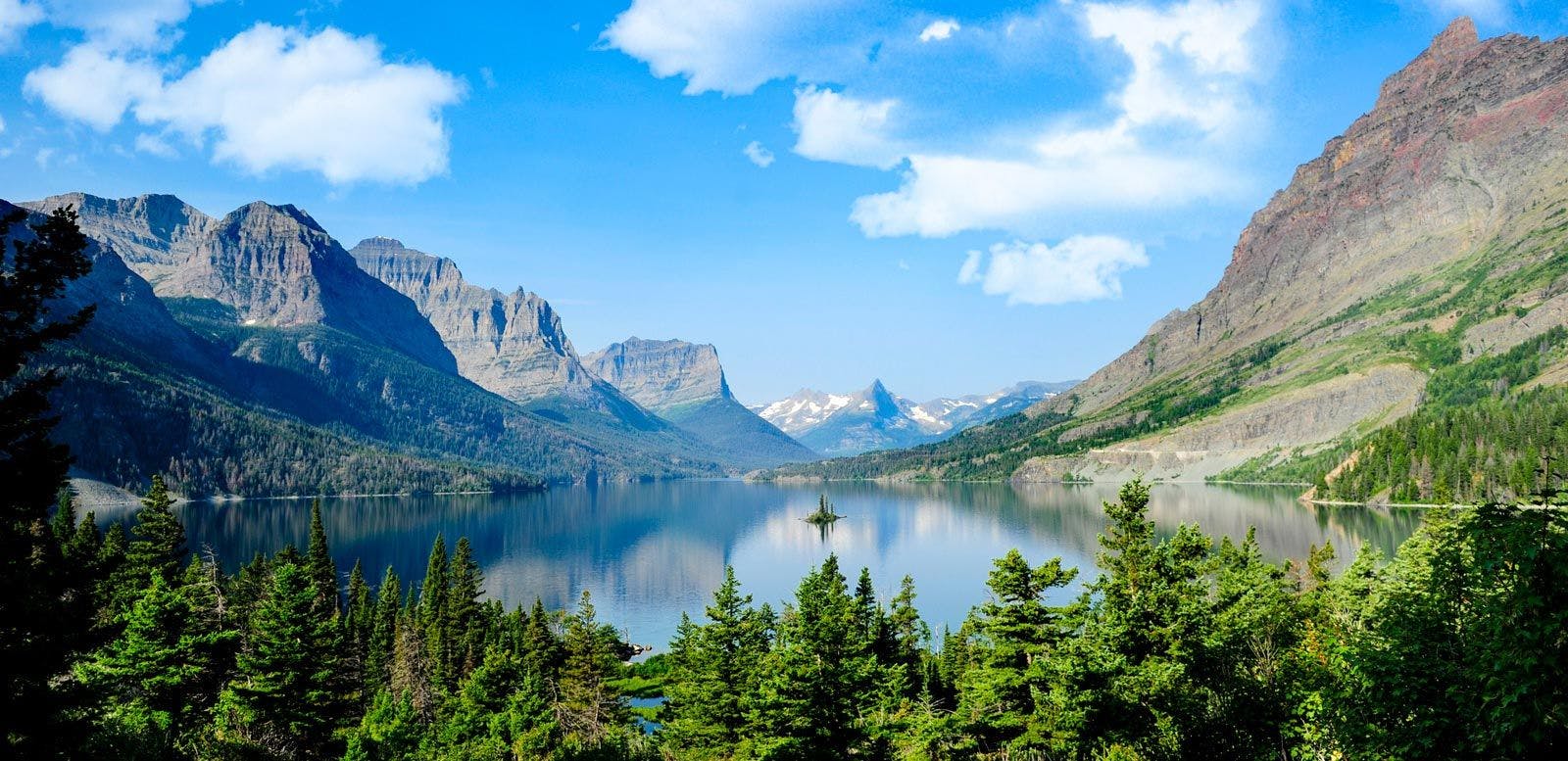 View of Glacier National Park with steep mountains, green forests and a still lake