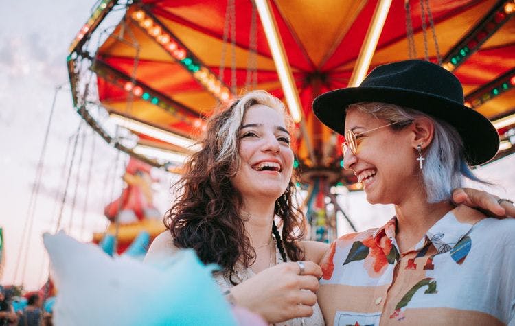Girlfriends embracing and laughing in front of theme park carousel