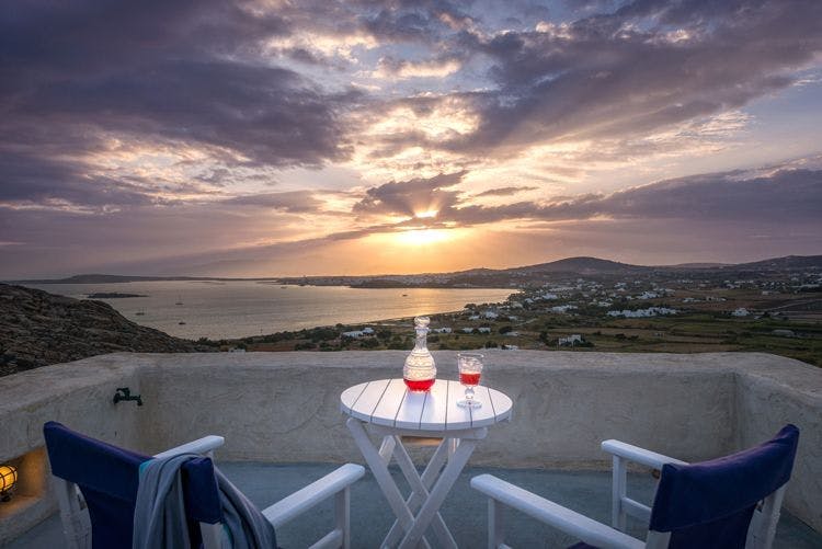 Paros luxury villas to rent with a view Villa Elxi outdoor seating area with two charis and table set with wine and view of the sea and coast