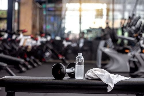Dumbbells, water bottle, and face towel on a bench in a gym
