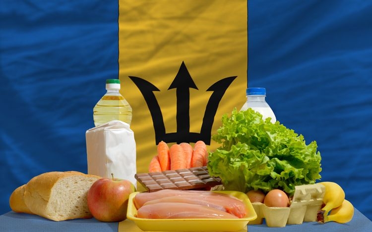 Various fresh groceries including chicken, bread, chocolate and milk in front of a Barbados flag